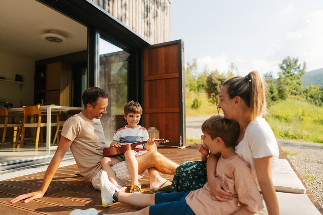 Family with two young boys enjoying the outdoors on the deck of home. One boy is playing a ukulele. - Benefits of reduced screen time