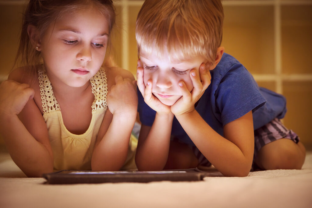 Two young kids lying on the floor looking at a tablet - kids and screen use