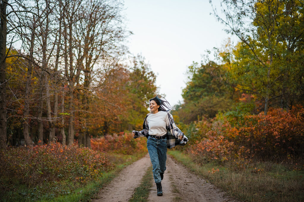 Beautiful brunette happy woman smiling while running in autumn forest