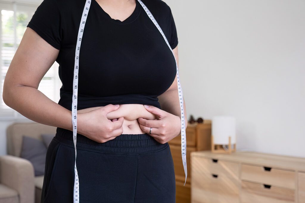 Woman pinching extra weight around her waist - stress and weight gain