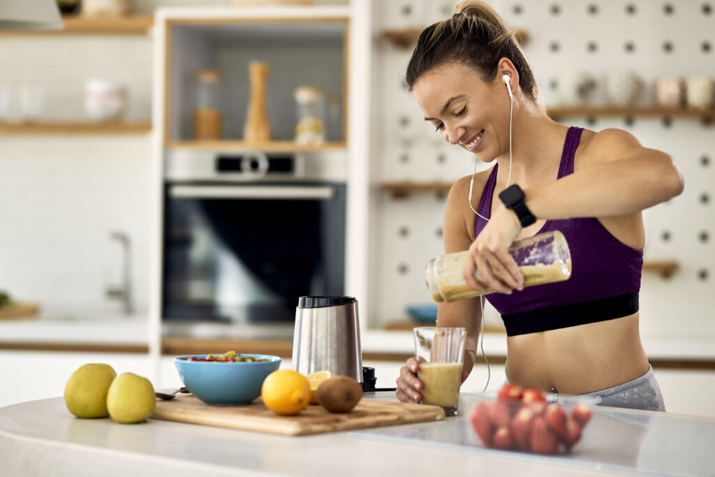 Young happy athletic woman having a fruit smoothie for breakfast in the kitchen. Tips for creating a balanced diet