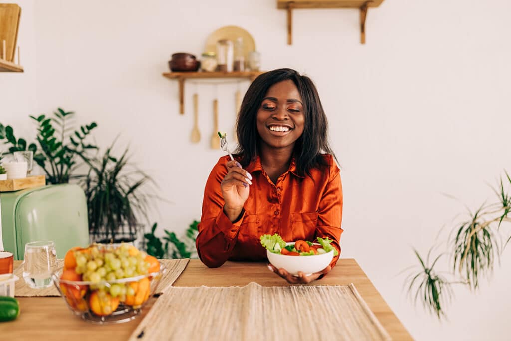 Woman happily eating a salad at kitchen table - how to eat slower