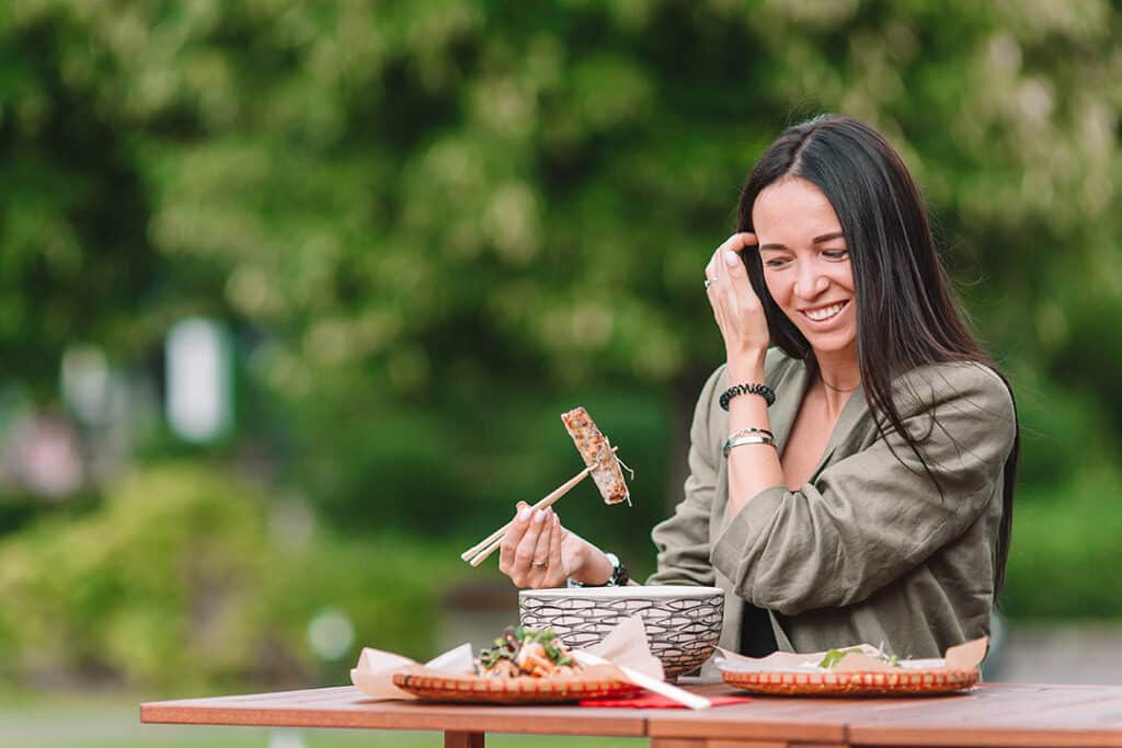 Woman eating food at an outdoor cafe with chopsticks - how to eat slower and improve digestion