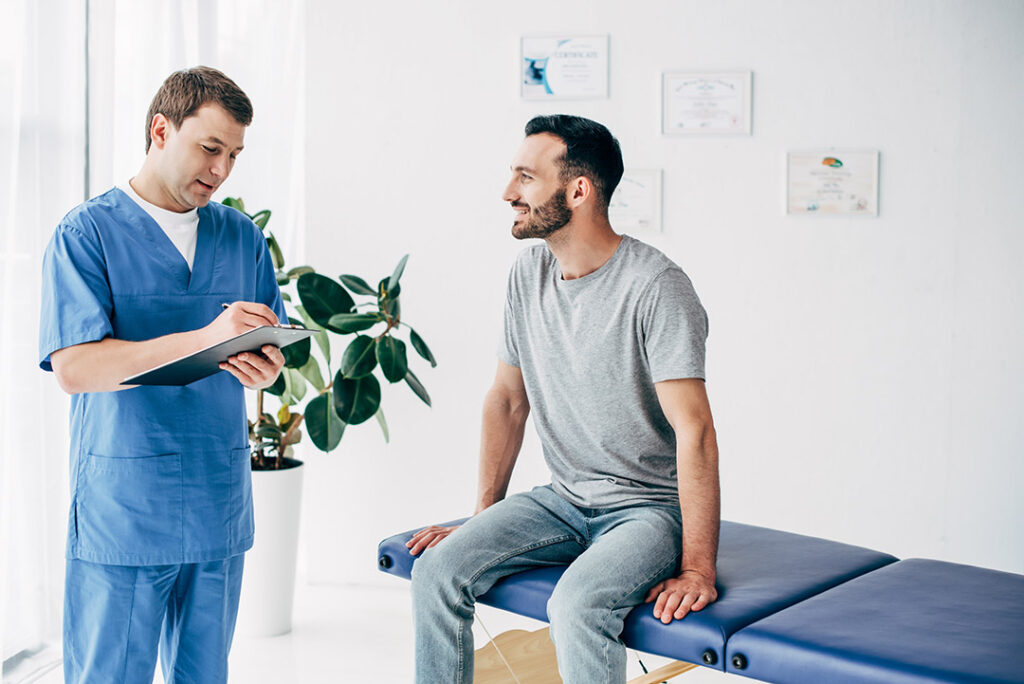 Smiling patient sitting on exam table talking with chiropractor