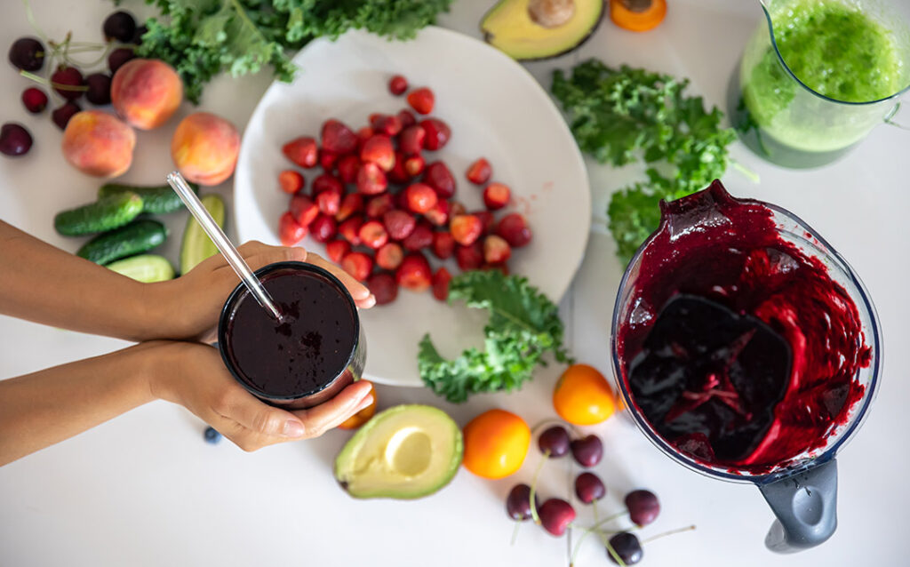 A glass with a berry smoothie in the hands of a woman. How to remove mold toxins in body.