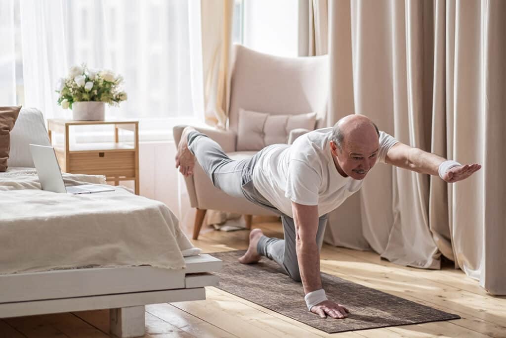 Senior caucasian men practices yoga asana chakravakasana for spine, bird pose at home during online lesson