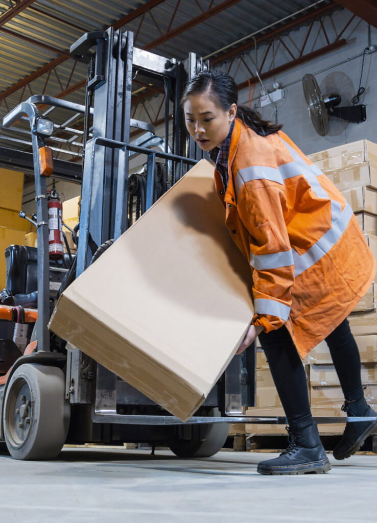 Woman lifting heavy box at warehouse - personal injury