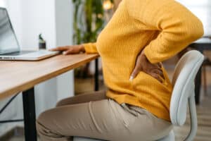 Woman working from home on a laptop with back pain