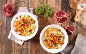 Two bowls of grains, roasted squash, herbs, and pomegranate seeds