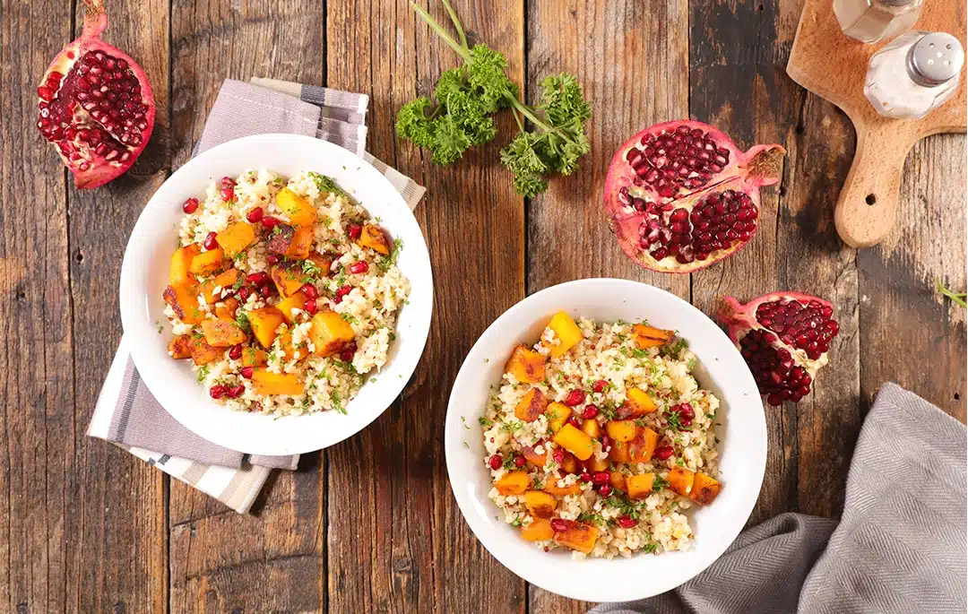 Two bowls of grains, roasted squash, herbs, and pomegranate seeds