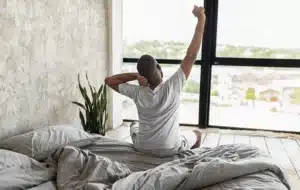 Person sitting on a bed and stretching beside a bright window