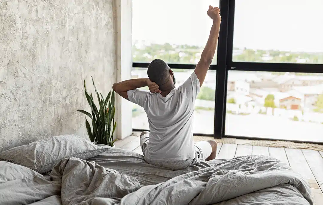Person sitting on a bed and stretching beside a bright window